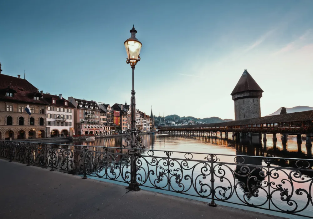 Im Hintergrund ist die Kapellbrücke in Luzern abends in der Dämmerung sichtbar, im Vordergrund steht eine Aussenbeleuchtung in Form einer Strassenlaterne