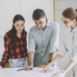 Zwei Frauen und ein Mann an einem Tisch. Die Mitarbeiterin von ewl zeigt einem Paar auf einem Plan die Realisierung einer PV-Anlage auf