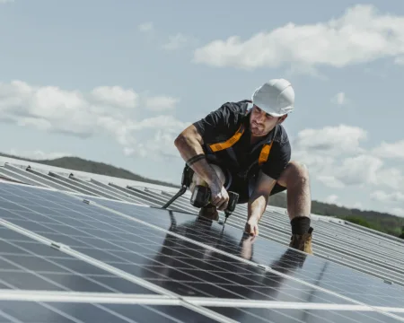 Ein Solarmonteur installiert Solarpanels auf einem Hausdach. Im Hintergrund ist der blaue Himmel mit einzelnen weissen Wolken zu sehen.