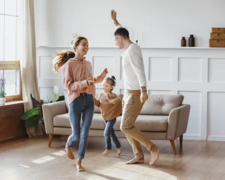 Eine Familie – Mutter, Vater, Tochter – tanzt im Wohnzimmer. Dank ihrer Heizung sind alle drei barfuss.