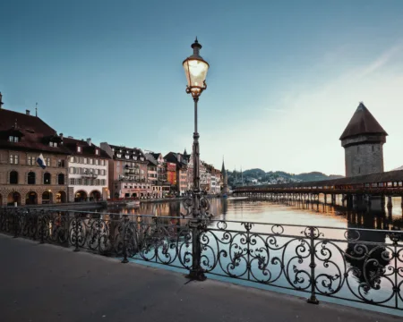 Im Hintergrund ist die Kapellbrücke in Luzern abends in der Dämmerung sichtbar, im Vordergrund steht eine Aussenbeleuchtung in Form einer Strassenlaterne