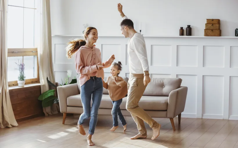 Eine Familie – Mutter, Vater, Tochter – tanzt im Wohnzimmer. Dank ihrer Heizung sind alle drei barfuss.